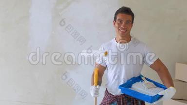 微笑的帅哥在家用滚筒画墙。 维修、建筑和家居概念